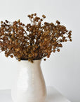 Three bundles of faux brown baby's breath filling a white container