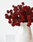Three faux red sedum bundles arranged together in a small vessel