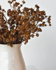 Faux dried gypsophila bundles in a white vessel showing depth of brown color