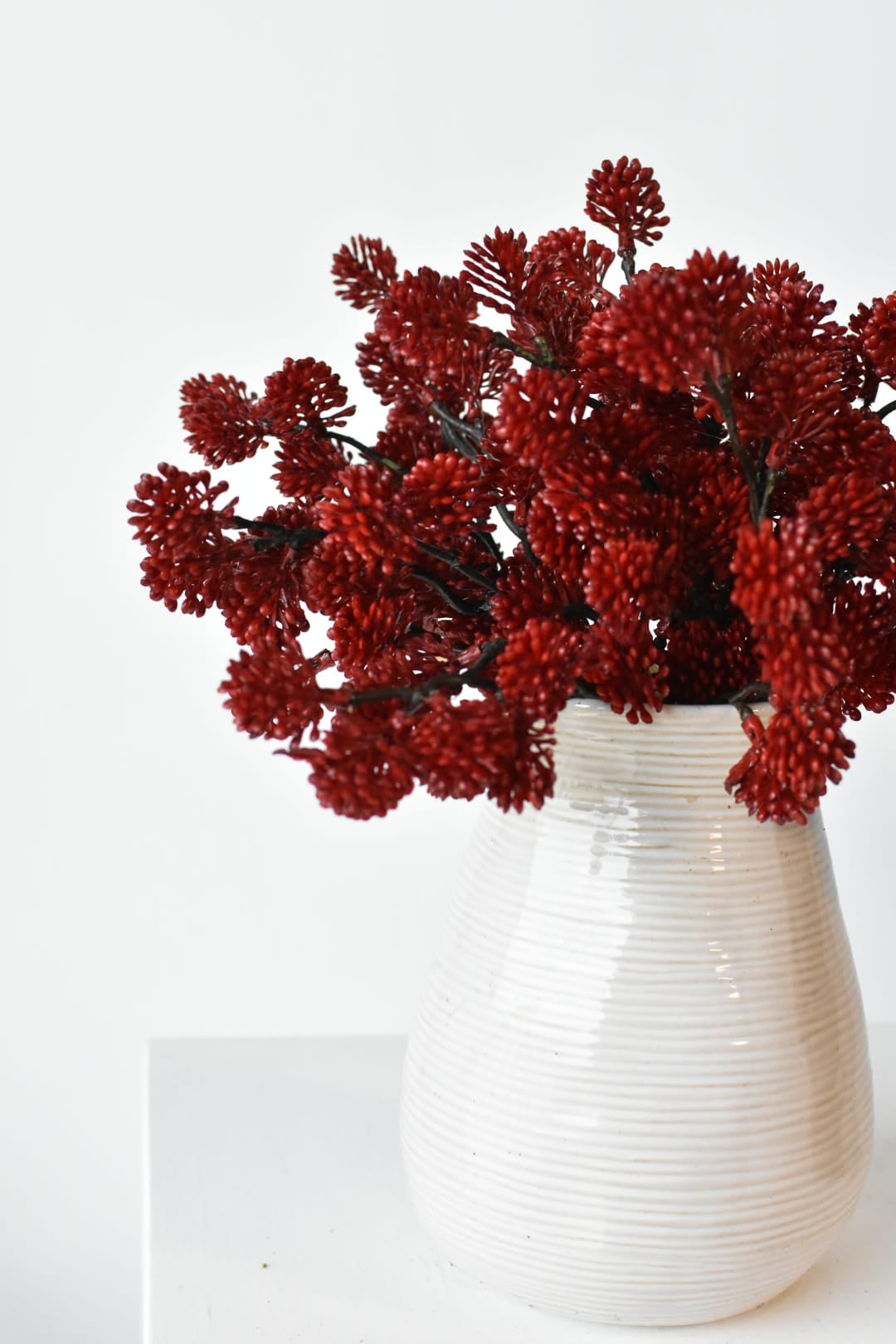 Three faux red sedum bundles arranged together in a small vessel