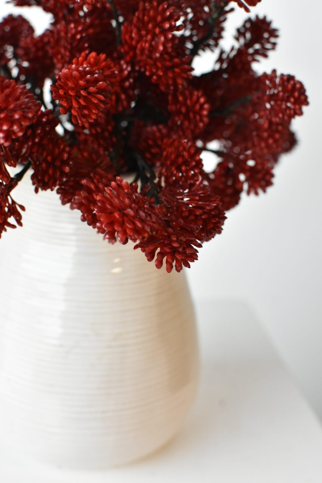 Three faux red sedum bundles filling a low container for a fall arrangement