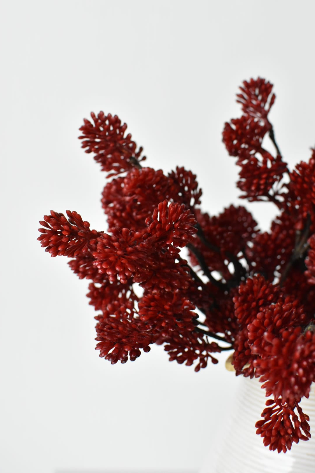 Faux red sedum bundles in a vessel showing depth of color across the clusters