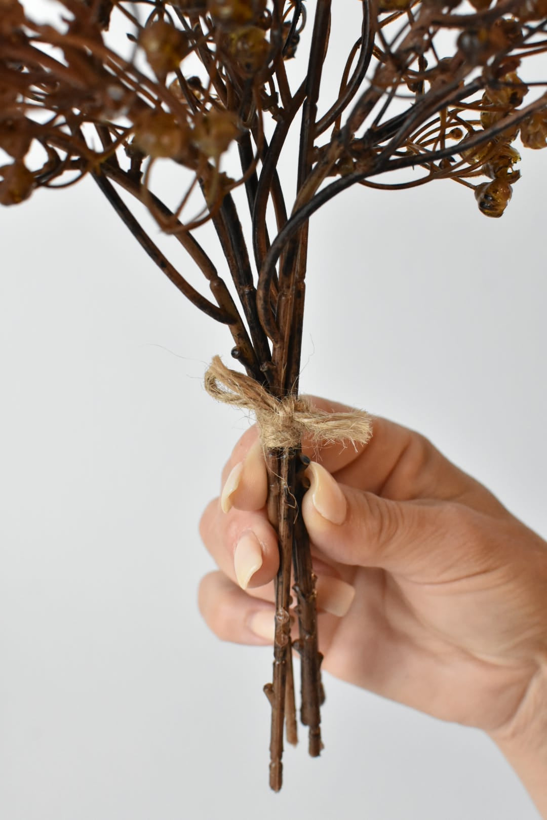 Faux dried baby's breath bundle in hand showing the twine tie at the base