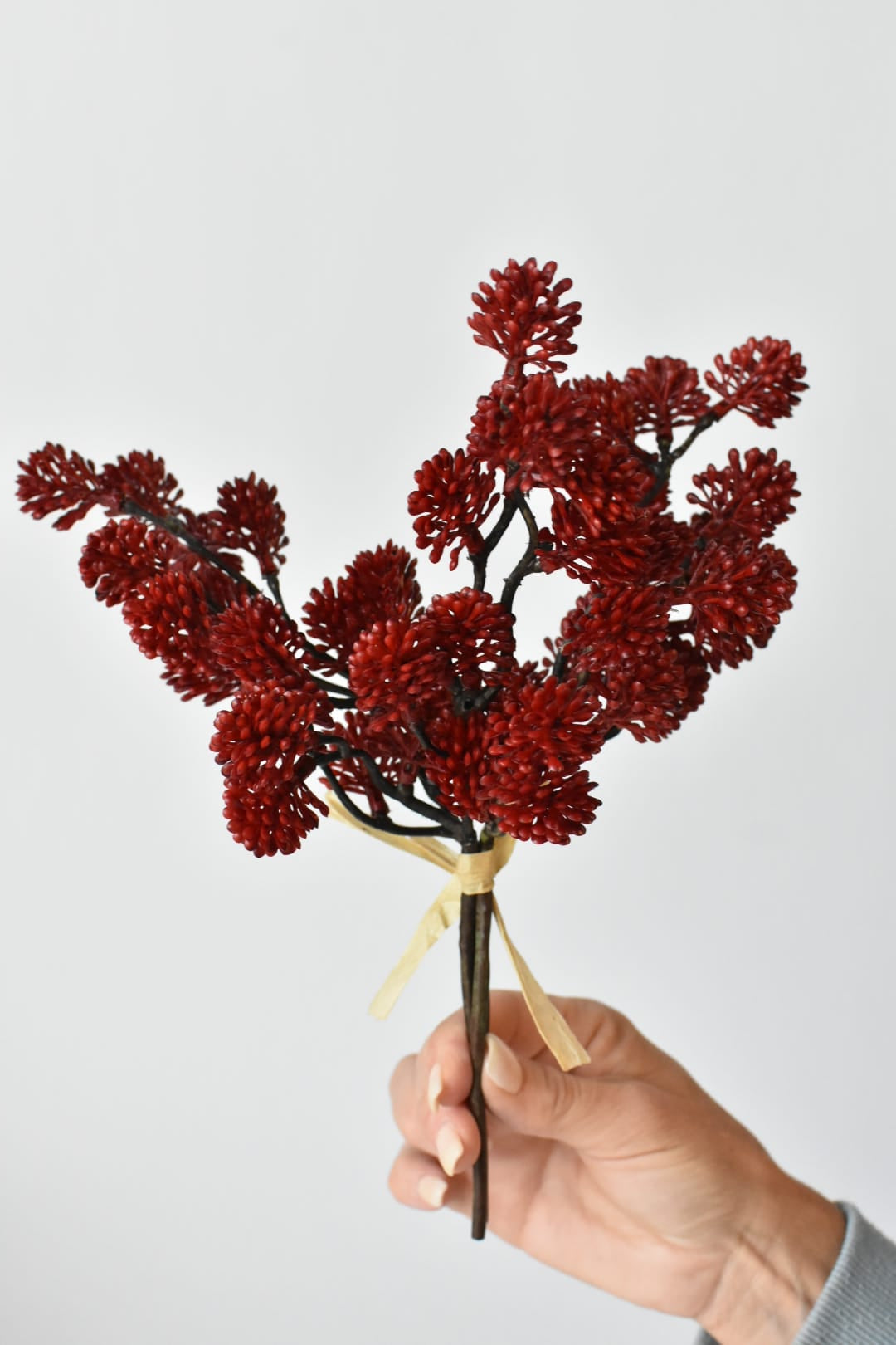 Hand holding an 11-inch faux red sedum stem bundle