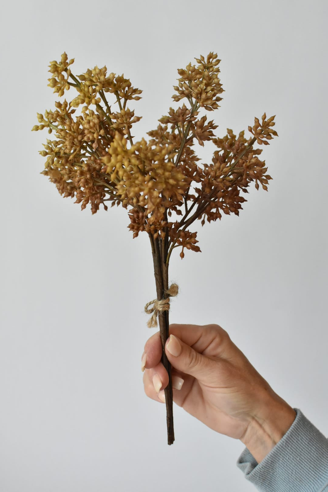 Hand holding a 12-inch faux beige sedum stem bundle