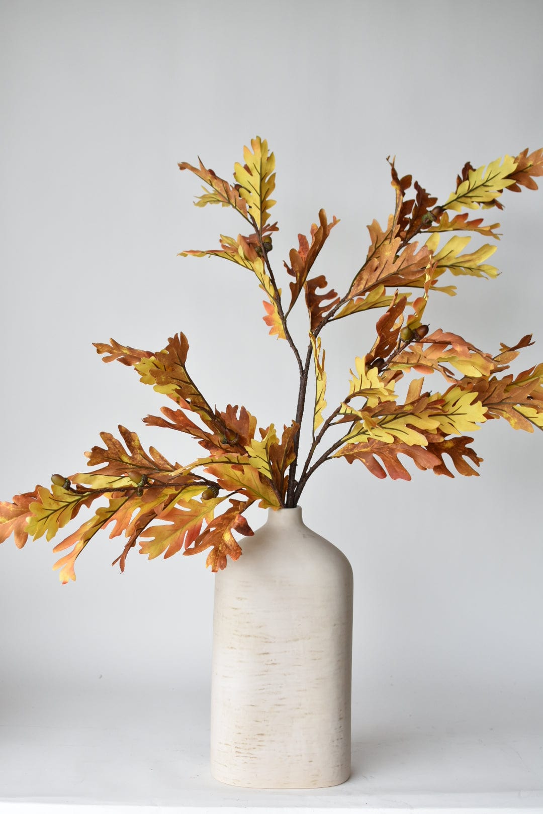 Three faux oak leaf branches in a tall vase